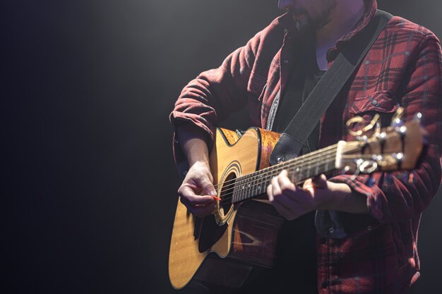 Músico masculino tocando la guitarra acústica en un espacio de copia de habitación oscura.