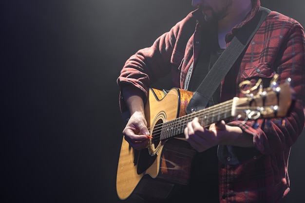 Músico masculino tocando la guitarra acústica en un espacio de copia de habitación oscura.