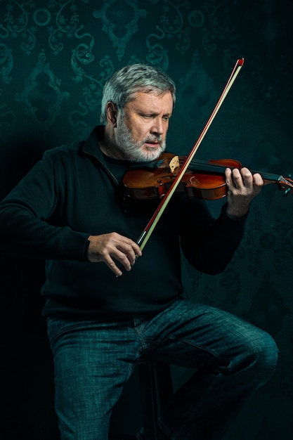 Músico senior tocando un violín con varita en negro
