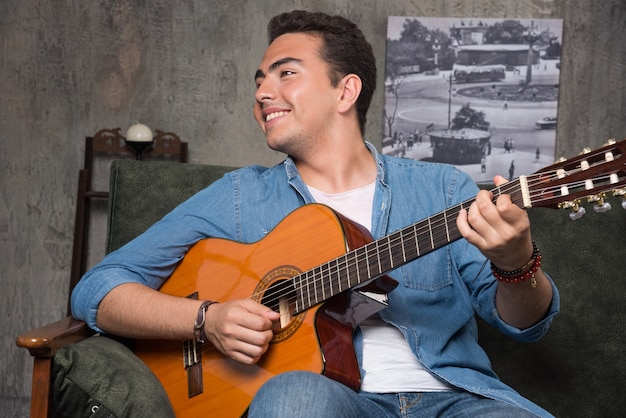 Músico sonriente tocando la guitarra y sentado en el sofá. Foto de alta calidad