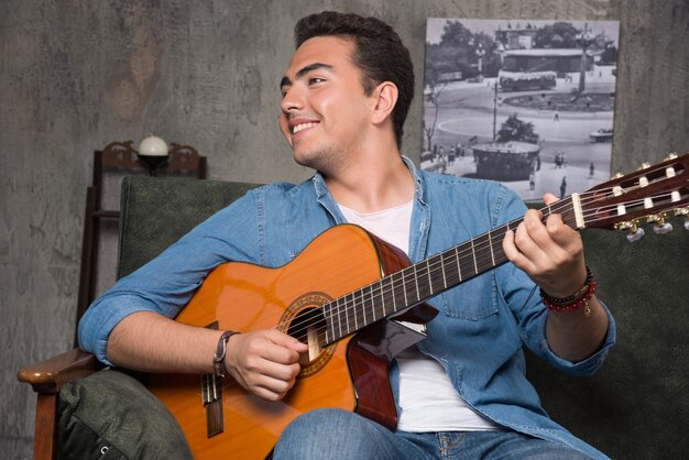 Músico sonriente tocando la guitarra y sentado en el sofá. Foto de alta calidad
