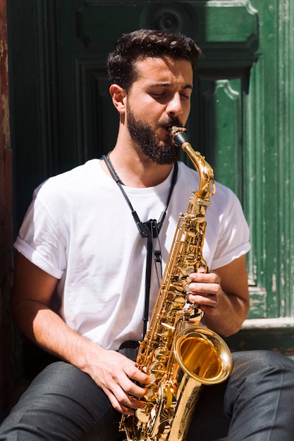 Músico de tiro medio sentado y tocando el saxo.