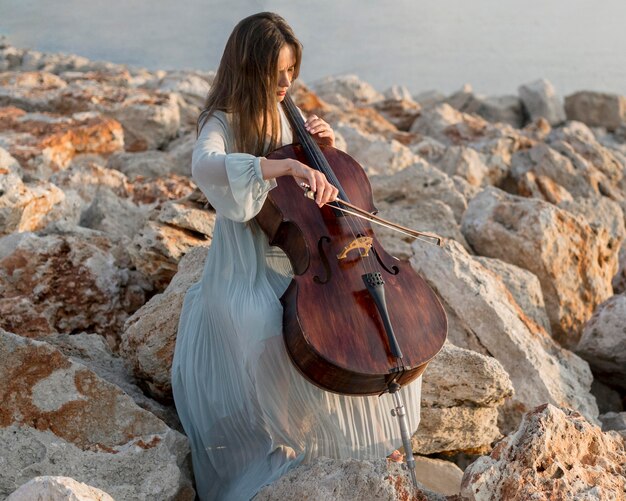 Músico tocando el violonchelo en las rocas al aire libre