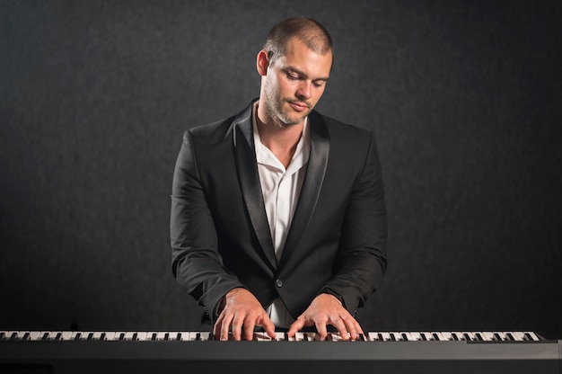 Músico vestido elegante tocando teclados y mirando el instrumento