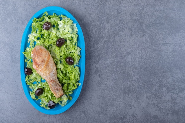 Muslo de pollo, aceitunas y lechuga en placa azul.