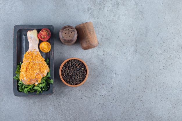 Muslo de pollo adobado en una tabla junto al cuenco de especias, sobre el fondo de mármol.