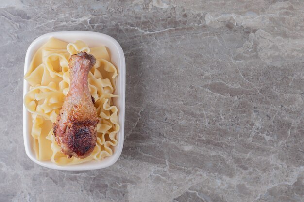 Muslo de pollo al horno sobre pasta, sobre el fondo de mármol.