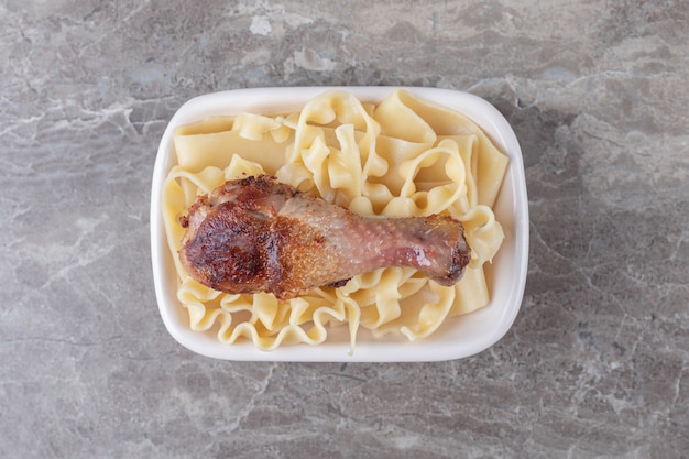 Muslo de pollo al horno sobre pasta, sobre el mármol.