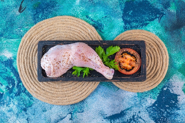 Foto gratuita muslo de pollo crudo marinado con tomates en una placa de madera sobre el salvamanteles