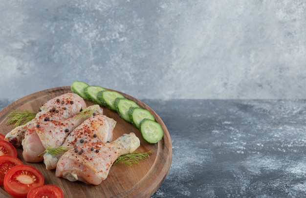 Muslo de pollo crudo marinado con verdura sobre tabla de madera.