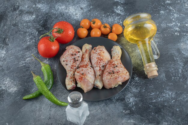 Muslo de pollo crudo en placa negra con verduras frescas y especias.