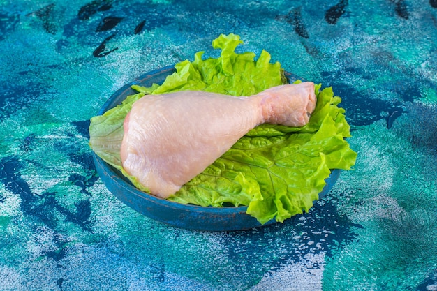 Muslo de pollo crudo sobre una lechuga en un plato