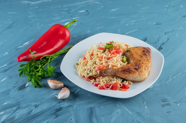 Muslo de pollo y fideos en un plato junto a verduras, sobre la superficie de mármol.