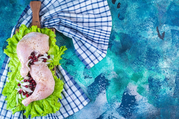 Foto gratuita muslo de pollo marinado con arilos de granada sobre hojas de lechuga sobre una placa sobre un paño de cocina sobre el fondo azul. foto de alta calidad