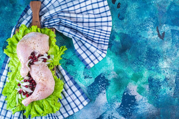 Muslo de pollo marinado con arilos de granada sobre hojas de lechuga sobre una placa sobre un paño de cocina sobre el fondo azul. Foto de alta calidad