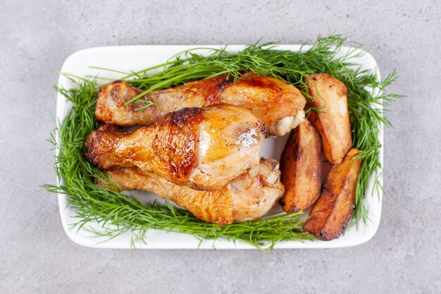 Muslos de pollo al horno con verduras en una placa blanca.