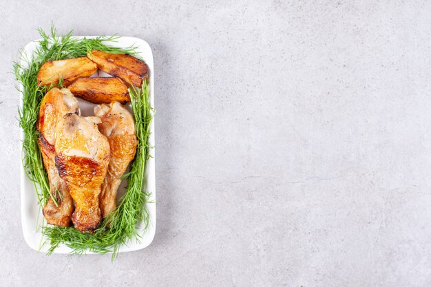 Muslos de pollo al horno con verduras en una placa blanca.