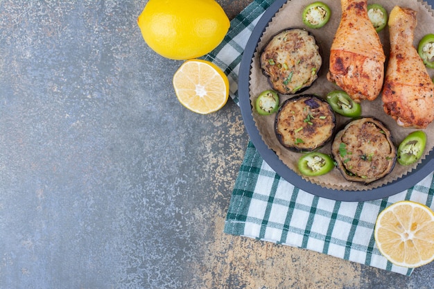 Muslos de pollo asado con verduras fritas y limón en tablero oscuro. Foto de alta calidad