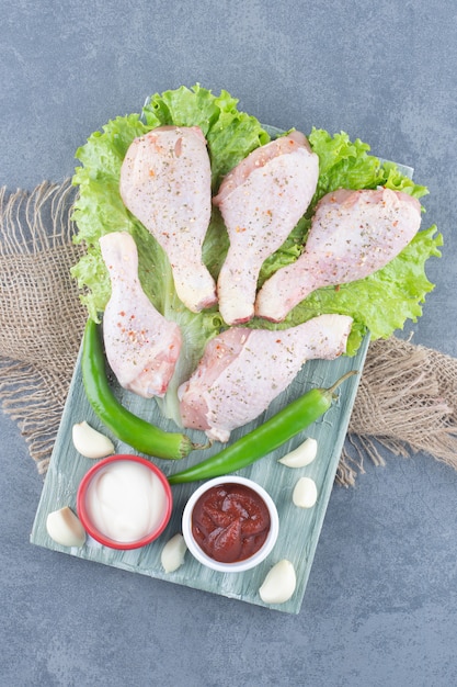 Muslos de pollo crudo y chiles sobre tabla de madera.