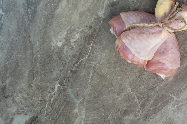Muslos de pollo crudo en cuerda sobre fondo de mármol. Foto de alta calidad