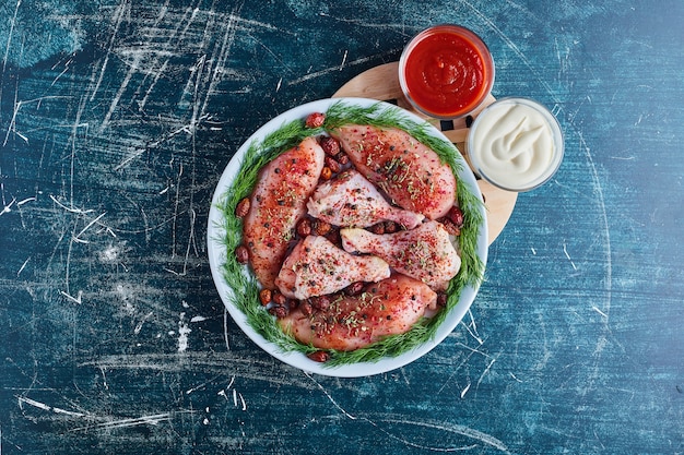 Muslos de pollo crudo con especias con salsa de tomate y mayonesa.