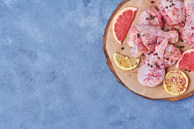 Muslos de pollo crudo con especias sobre una tabla de madera en azul