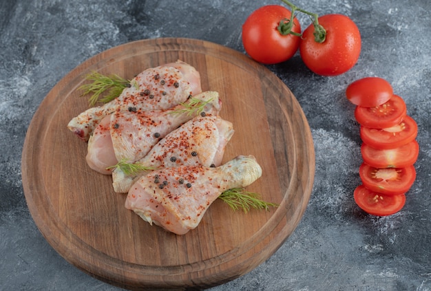 Muslos de pollo crudo con especias y tomates enteros o en rodajas sobre una tabla de madera.