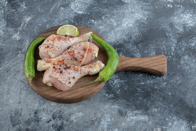 Muslos de pollo crudo orgánico fresco y pimientos verdes sobre una tabla de cortar de madera.