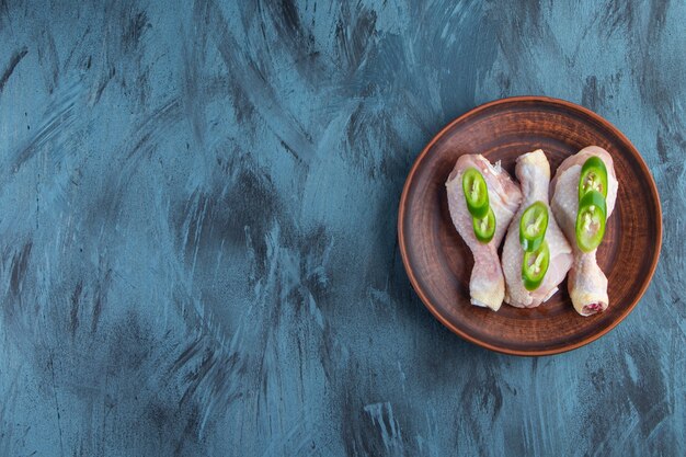 Muslos de pollo crudo y pimiento en rodajas en un plato, sobre el fondo azul.