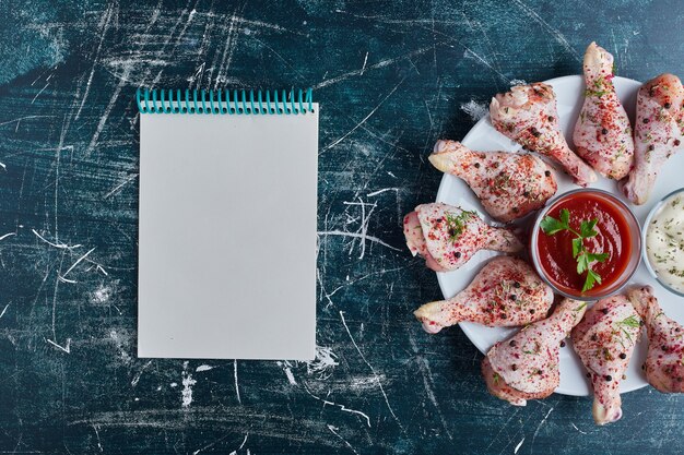 Muslos de pollo crudo en un plato blanco con un libro de recetas a un lado.