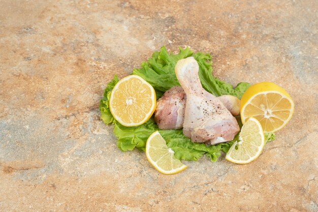 Muslos de pollo crudo con rodajas de limón y lechuga sobre superficie de mármol