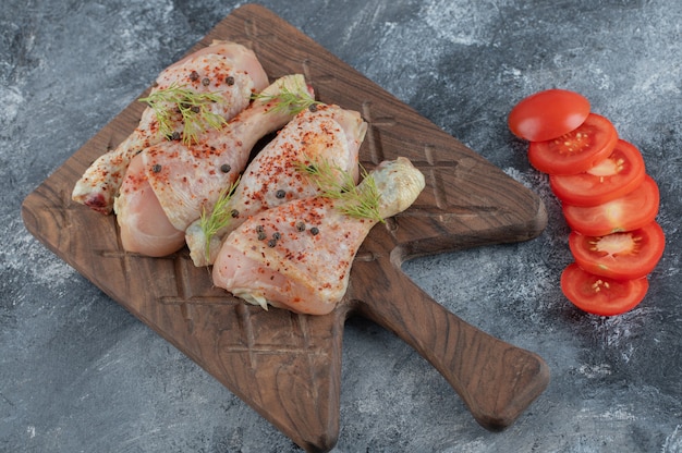 Muslos de pollo crudo y rodajas de tomate orgánico en el tablero de la cocina.