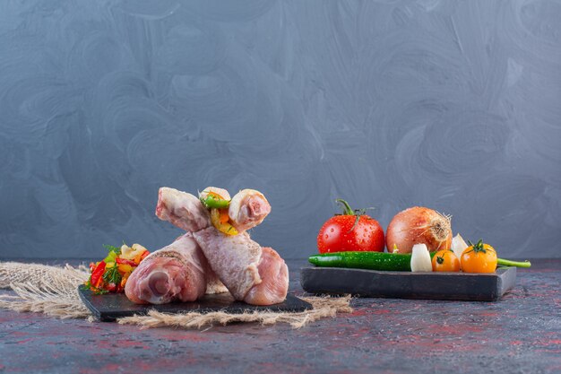 Muslos de pollo crudo sobre tabla de cortar negra con verduras