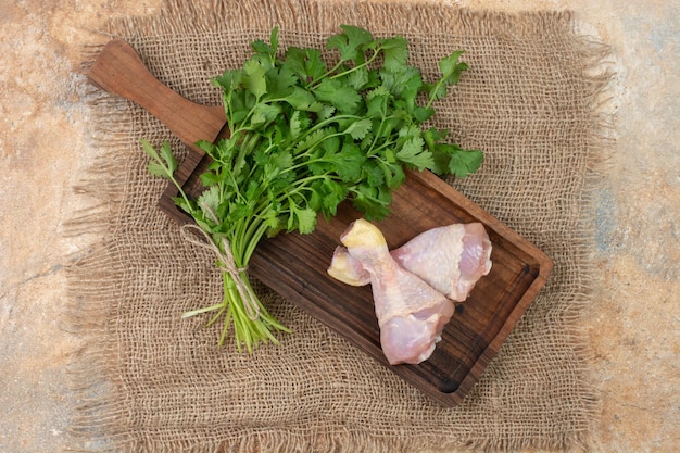 Muslos de pollo crudo con verduras sobre tabla de cortar de madera sobre tela de saco.