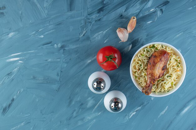 Muslos de pollo y fideos en un recipiente junto a la sal, los tomates y el ajo, sobre el fondo de mármol.