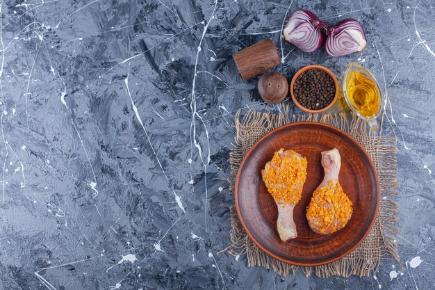 Muslos de pollo marinado en un plato sobre una arpillera junto a especias y cebolla en la superficie azul