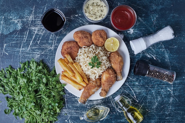 Muslos de pollo y patatas fritas con fideos y salsas.