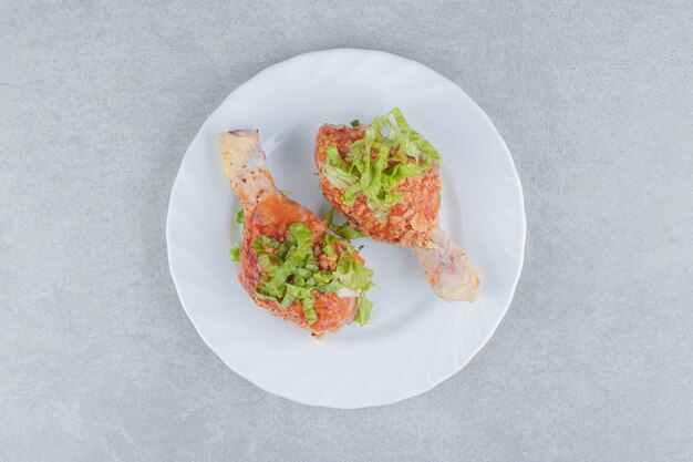 Muslos de pollo picante crudo en el plato, sobre la superficie blanca