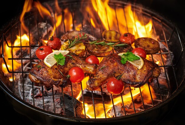 Muslos de pollo a la plancha a la parrilla en llamas con verduras asadas con tomates, patatas, semillas de pimiento, sal.