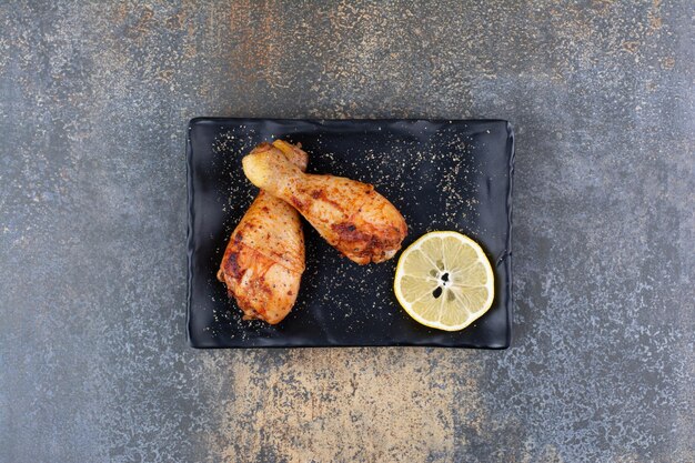 Muslos de pollo a la plancha en placa negra con limón. Foto de alta calidad