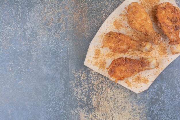 Muslos de pollo a la plancha sobre tabla de madera con pan rallado. Foto de alta calidad