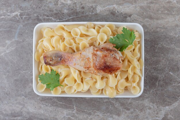 Muslos de pollo sobre pasta en el bol, sobre el mármol.