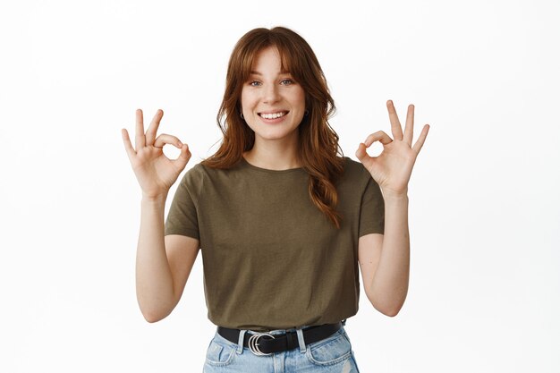 Muy bien, buen trabajo. Mujer joven sonriente que muestra el gesto de Ok, ok, asiente con la cabeza en señal de aprobación, diga que sí, de acuerdo con su elección, elogie lo grandioso, de pie en blanco