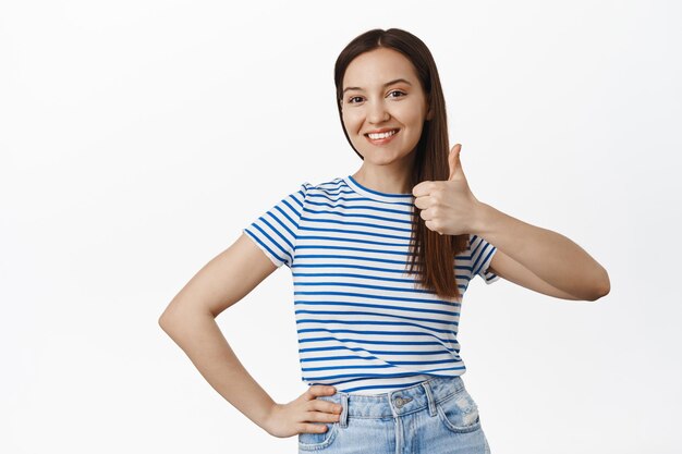 Muy bien. Una mujer sonriente y satisfecha de 20 años muestra el pulgar hacia arriba y asiente con aprobación, recomienda algo, deja comentarios positivos sobre la empresa o el servicio, le gusta y alaba algo excelente.