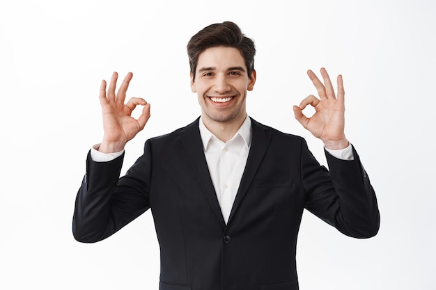 Muy bien. Sonriente hombre de negocios satisfecho, empresario masculino en traje de negocios, muestra signos de aprobación y asiente con la cabeza, dice que sí, está de acuerdo y elogia el trabajo, fondo blanco.