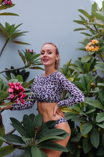 Muy bonita mujer caucásica con cuerpo perfecto en traje de baño de leopardo con hermosas flores tropicales