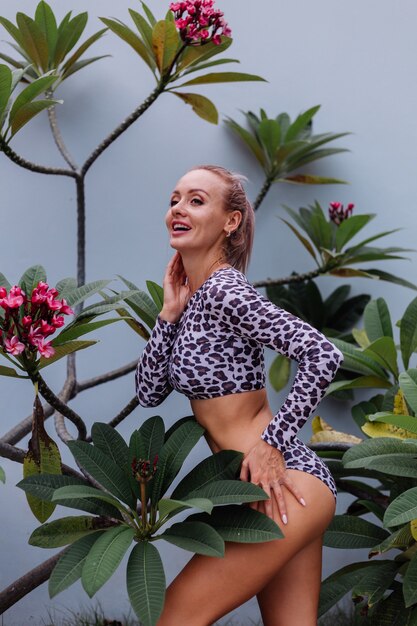 Muy bonita mujer caucásica con cuerpo perfecto en traje de baño de leopardo con hermosas flores tropicales