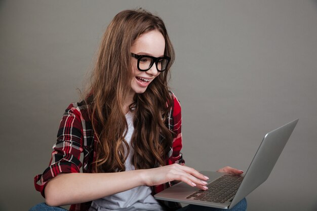 Muy sonriente jovencita chateando por computadora portátil