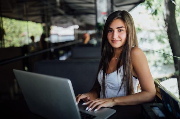 Muy sonriente niña trabaja en su computadora portátil en la terraza del café daytilme