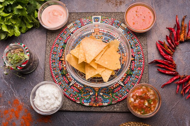 Nachos junto a la pimienta y la salsa en tazones colocados en una bandeja creativa